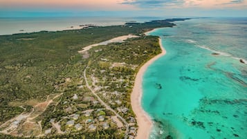 An aerial view of a coastal area with a beach, clear turquoise waters, and a mix of residential and natural landscapes.