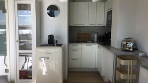 A compact kitchen with white cabinets, a small refrigerator, a coffee maker, and a toaster. - Holiday Apartment Hammerle-seiler (Ueberlingen)