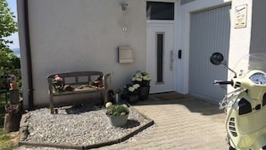 A paved patio with a bench, potted plants, and a scooter parked in front of a building with a garage door. - Holiday Apartment Hammerle-seiler (Ueberlingen)