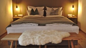 Un lit bien fait, recouvert d’une couverture blanche et agrémenté de deux oreillers, un tapis blanc et moelleux posé sur une table en bois, et deux lampes de chevet sur des tables de nuit.