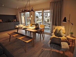 A modern living room with a dining area, wooden flooring, and a large window offering a view of the outside. - Lively Apartment in Sonthofen (Sonthofen)