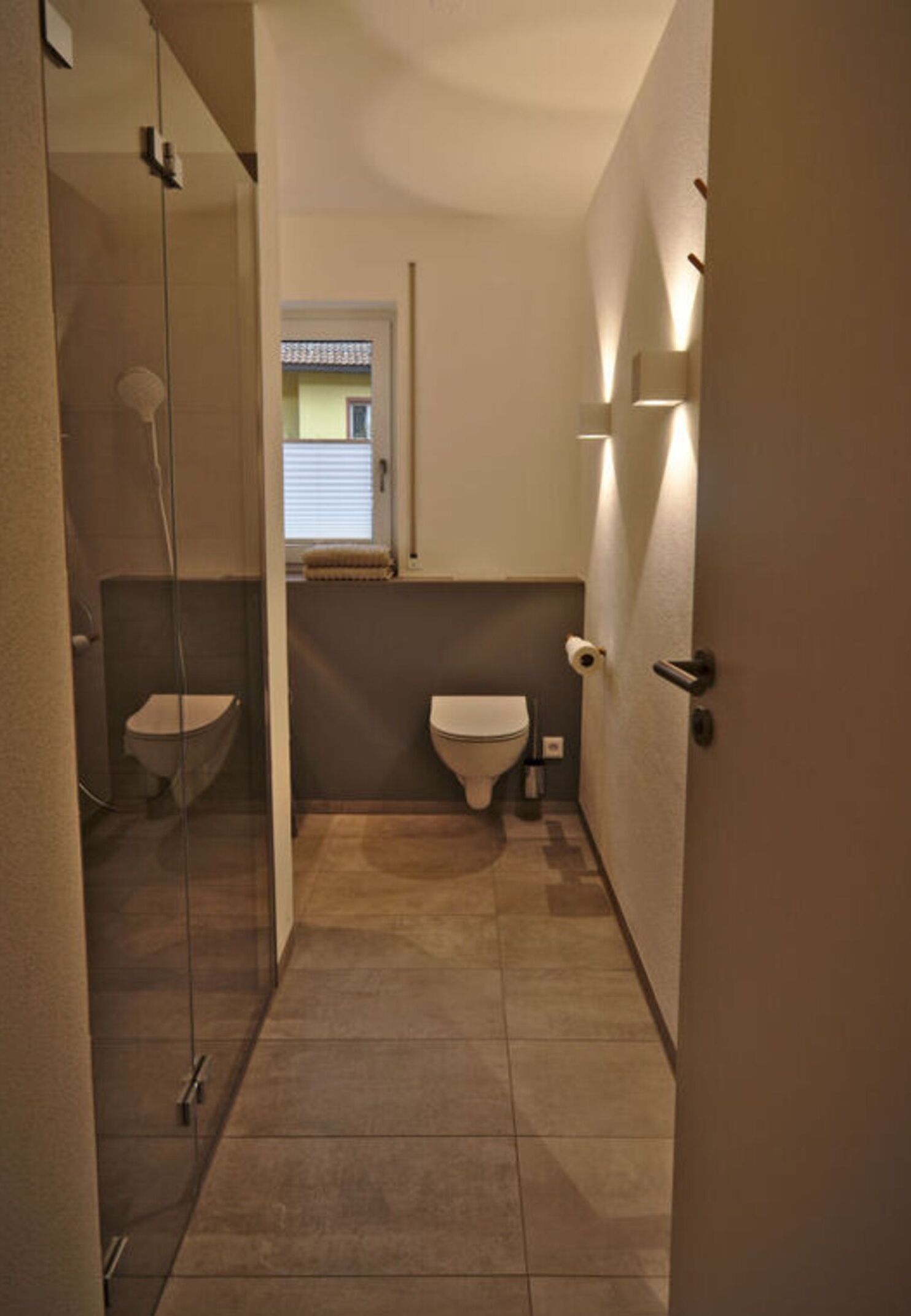Un baño estrecho con inodoro, zona de ducha y una pequeña ventana.