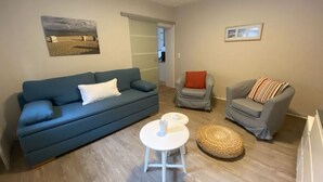 A living room with a blue sofa, a grey armchair, a white table, and a woven ottoman. - 2 Rena Modern Retreat (Sierksdorf)