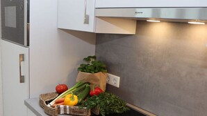 Une cuisine avec des meubles blancs, une hotte en acier inoxydable et une plaque de cuisson à induction noire.