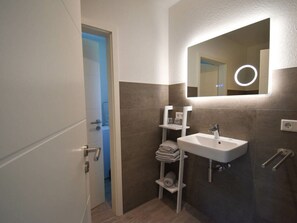 A modern bathroom with a white sink, a mirror with a light, and a towel rack. - My Baltic Sea Place House by the sea 9 (Niesgrau)