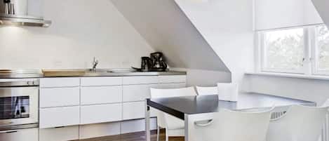 Una cocina moderna con armarios blancos, suelo de madera, una mesa de comedor con sillas y un ventanal que proporciona luz natural.