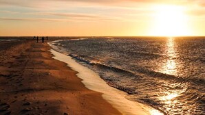 Una spiaggia al tramonto, con onde calme e alcune persone che camminano sulla riva.