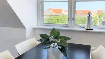 A dining area with a table and chairs, a potted plant, and a window with a view of houses.