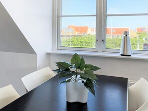 A dining area with a table and chairs, a potted plant, and a window with a view of houses. - 5 Star Holiday Home in Skagen (Skagen)