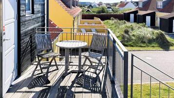 A balcony with a table and chairs, a view of neighboring houses, and a wooden deck.