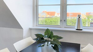 Zona pranzo con tavolo e sedie, una pianta in vaso e una finestra vista case.