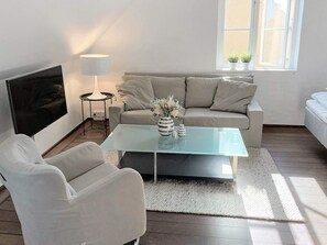 Ein modernes Wohnzimmer mit einer Couch, einem Glastisch, einem Fernseher und einer Lampe.