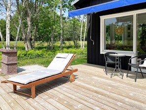 A wooden deck with a lounge chair and a table, a black building with large windows, and a natural backdrop of trees and grass. - 4 Star Holiday Home in Lottorp (Löttorp)