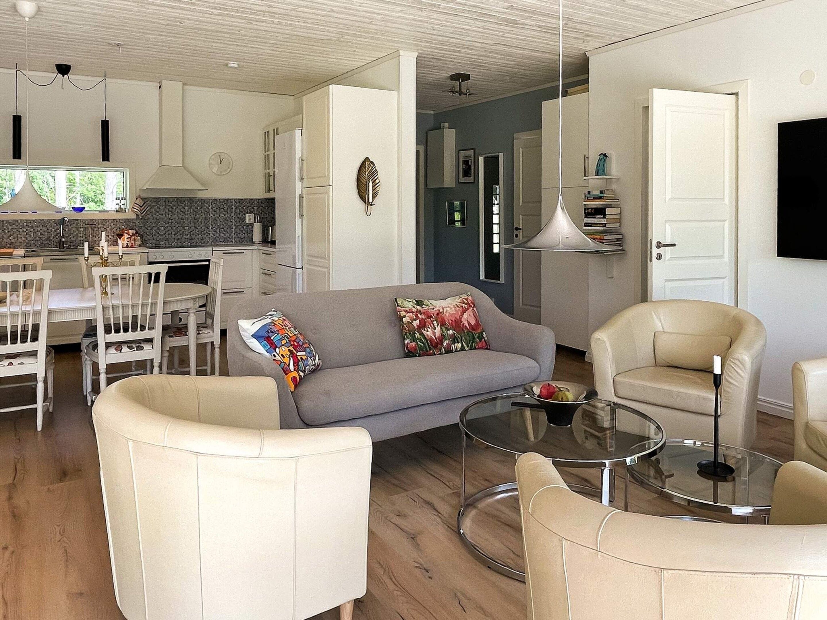 A modern living room with a grey sofa, beige armchairs, and a glass coffee table.