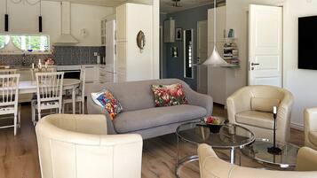 Una sala de estar moderna con un sofá gris, sillones color beige y una mesa de centro de vidrio.