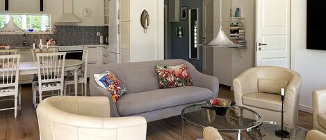 A modern living room with a grey sofa, beige armchairs, and a glass coffee table.