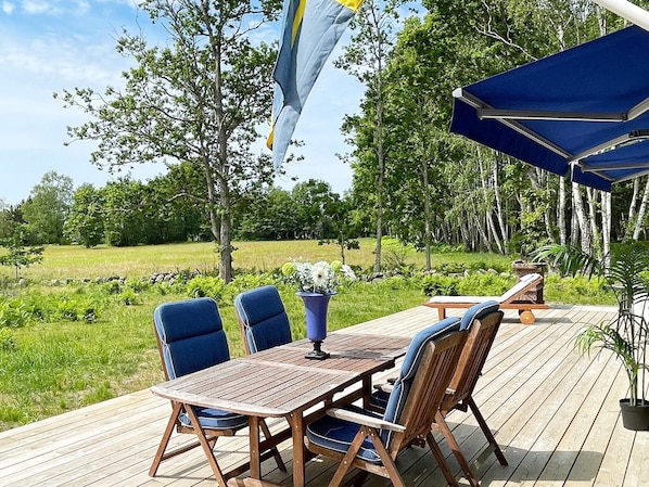 An outdoor dining area with a wooden table and chairs, surrounded by greenery and trees.