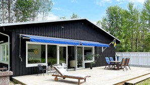 A black building with a wooden deck, outdoor seating, and a flag. - 4 Star Holiday Home in Lottorp (Löttorp)
