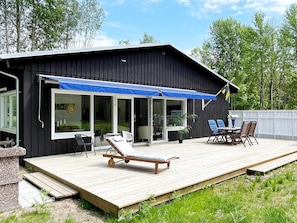 En sort bygning med en træterrasse, udendørs siddepladser og et flag.