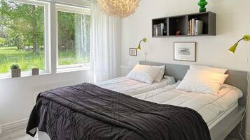 Un dormitorio con cama, una mesita de noche, una ventana con cortinas, una repisa en la pared con libros y una lámpara colgante.