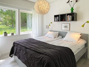A bedroom with a bed, a bedside table, a window with curtains, a wall-mounted shelf with books, and a hanging light fixture. - 4 Star Holiday Home in Lottorp (Löttorp)
