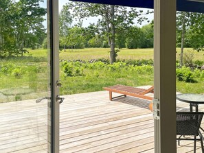 A wooden deck with a bench and a table, overlooking a grassy area with trees and a pond. - 4 Star Holiday Home in Lottorp (Löttorp)
