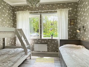 A room with two bunk beds, a radiator, a window with curtains, a plant, and a wall-mounted lamp. - 4 Star Holiday Home in Lottorp (Löttorp)