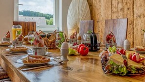 A breakfast table with various food items, a window with a view of trees, and a wooden wall. - History and Luxus (Schonach im Schwarzwald)