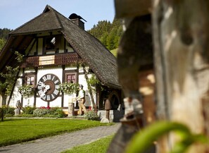 A traditional half-timbered building with a large clock, a well-maintained garden, and a clear pathway leading to the entrance. - History and Luxus (Schonach im Schwarzwald)