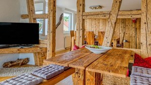 A rustic wooden interior with exposed beams, a wooden table with a bowl of fruit, and a television on a wooden stand. - History and Luxus (Schonach im Schwarzwald)