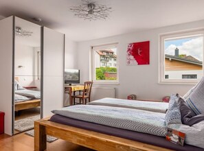 A bedroom with a bed, a desk with a computer, a chair, and a window with a view of buildings. - History and Luxus (Schonach im Schwarzwald)