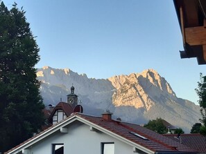 A building with a clock tower, surrounded by trees and mountains in the background. - Pleasant Holiday Home With View (Garmisch-Partenkirchen)