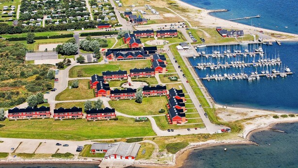 Vista aérea de uma área residencial costeira com um porto de iates, casas e uma estrada.