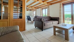 En rummelig opholdsstue med træloft, sofa, bord og udsigt til det fri.