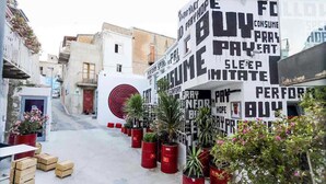 A narrow street with buildings on either side, potted plants, and a large wall with various words and phrases. - Belvilla by OYO Schembri Appartement (Agrigento)