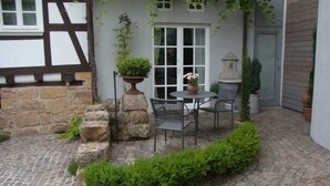 A stone-paved patio with a table and chairs, surrounded by greenery and a stone wall. - Pfaelzerleben (Oberotterbach)