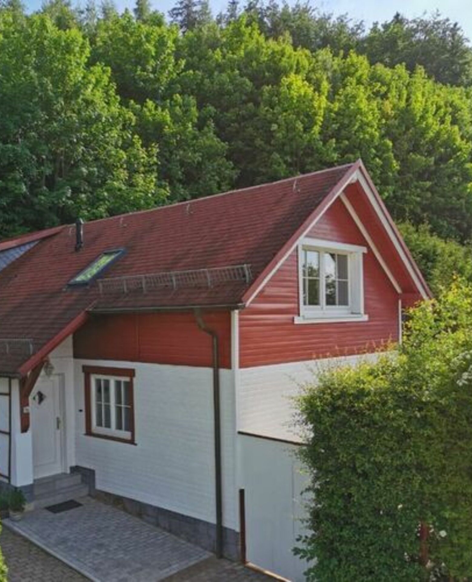 Une maison rouge et blanche avec un toit en pente, un petit porche et une fenêtre.
