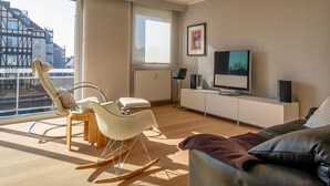 A modern living room with a large window, a television, and a cozy seating area. - Balcony Views & Comfort (De Haan)