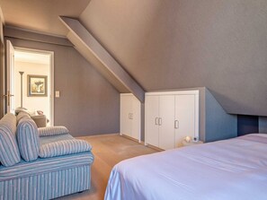 A bedroom with a sloped ceiling, a bed, a sofa, and a wardrobe. - Balcony Views & Comfort (De Haan)