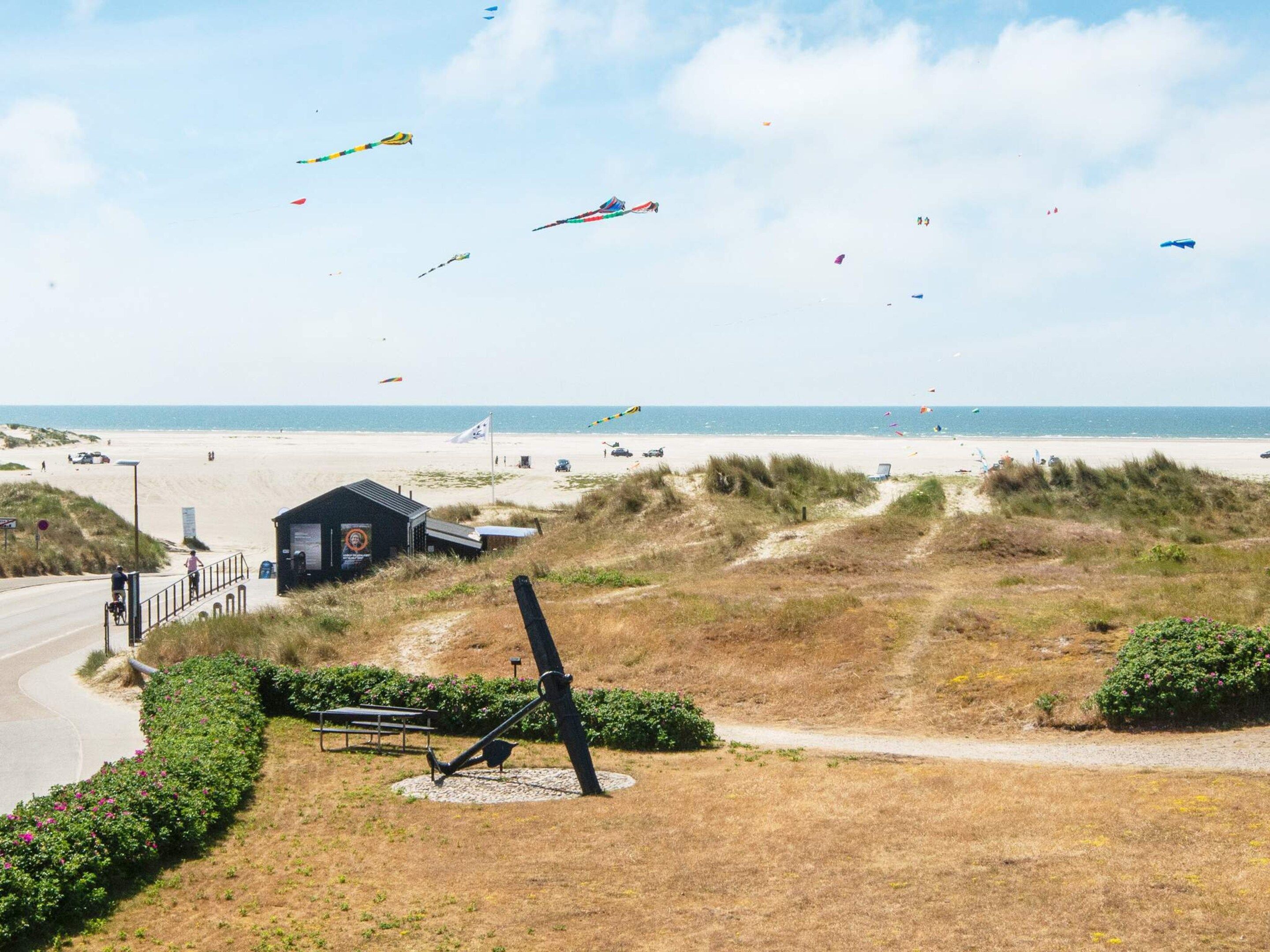 A beach with a path leading to a small building, a bench, and a sculpture.