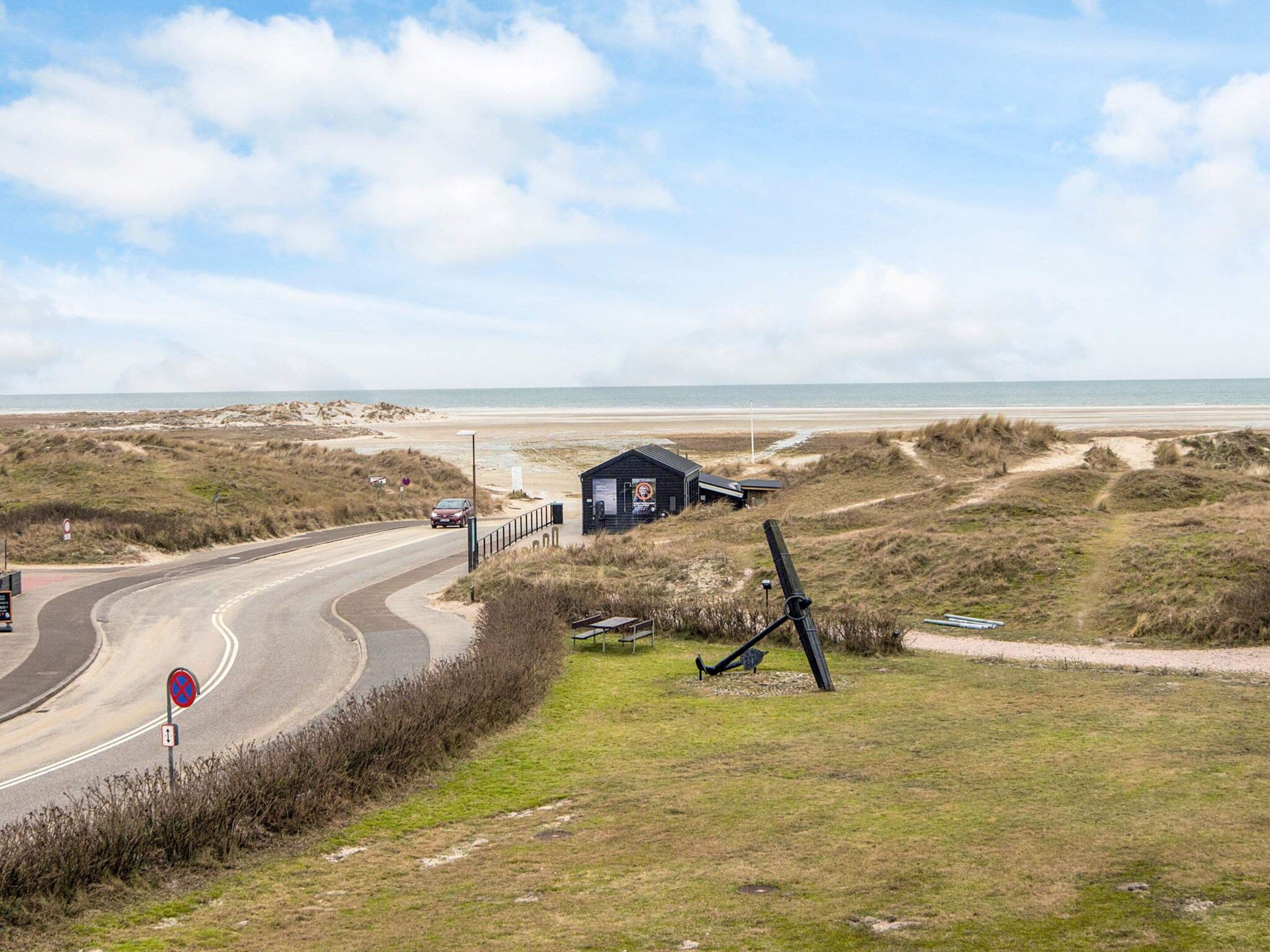A coastal road with a beach view, a small structure, and a directional sign.