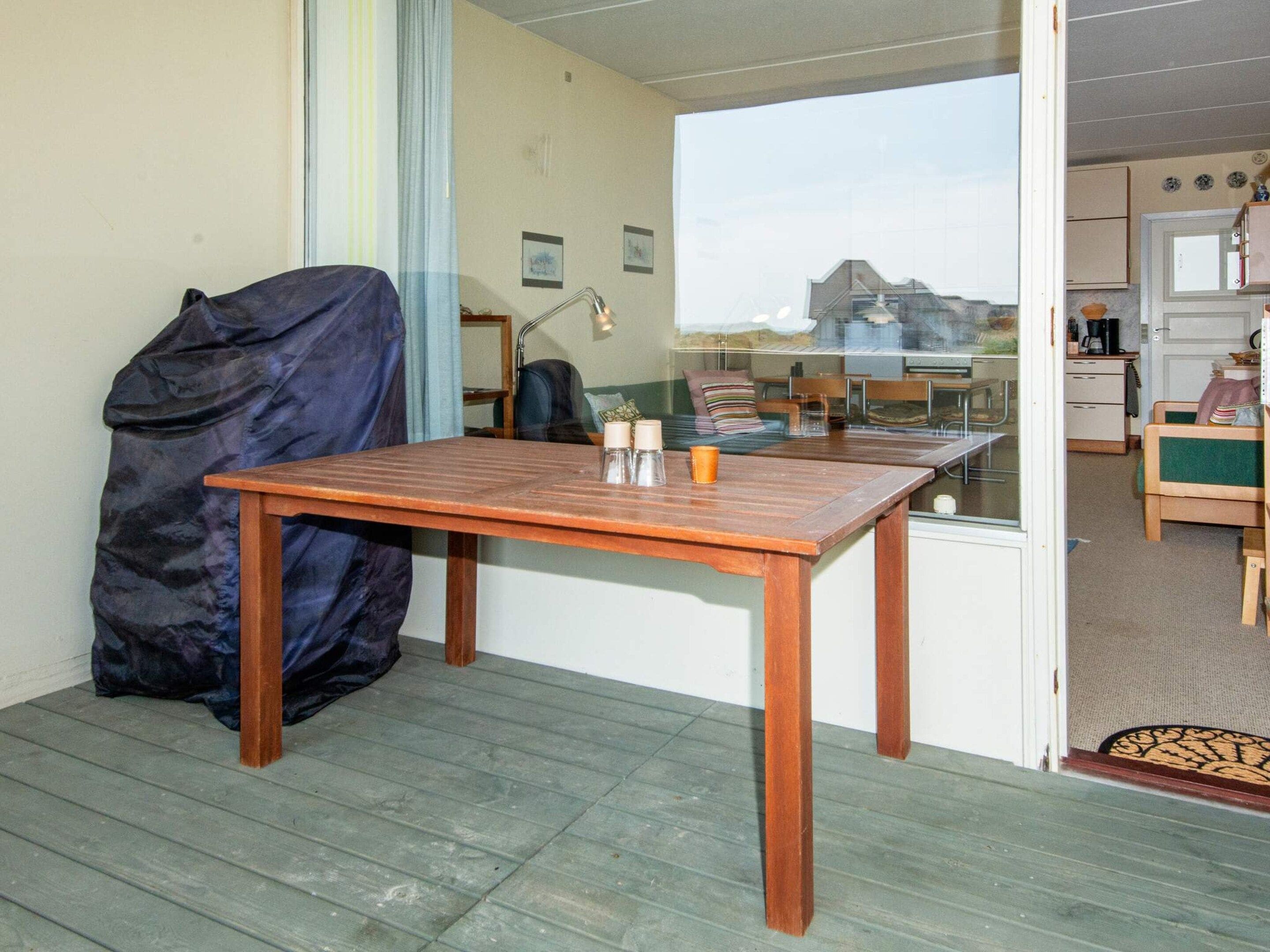 A room with a wooden table, a chair, a bed, a window, and a door leading to another room.