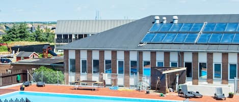Un edificio con piscina, paneles solares y un área cercada con sillones de descanso.