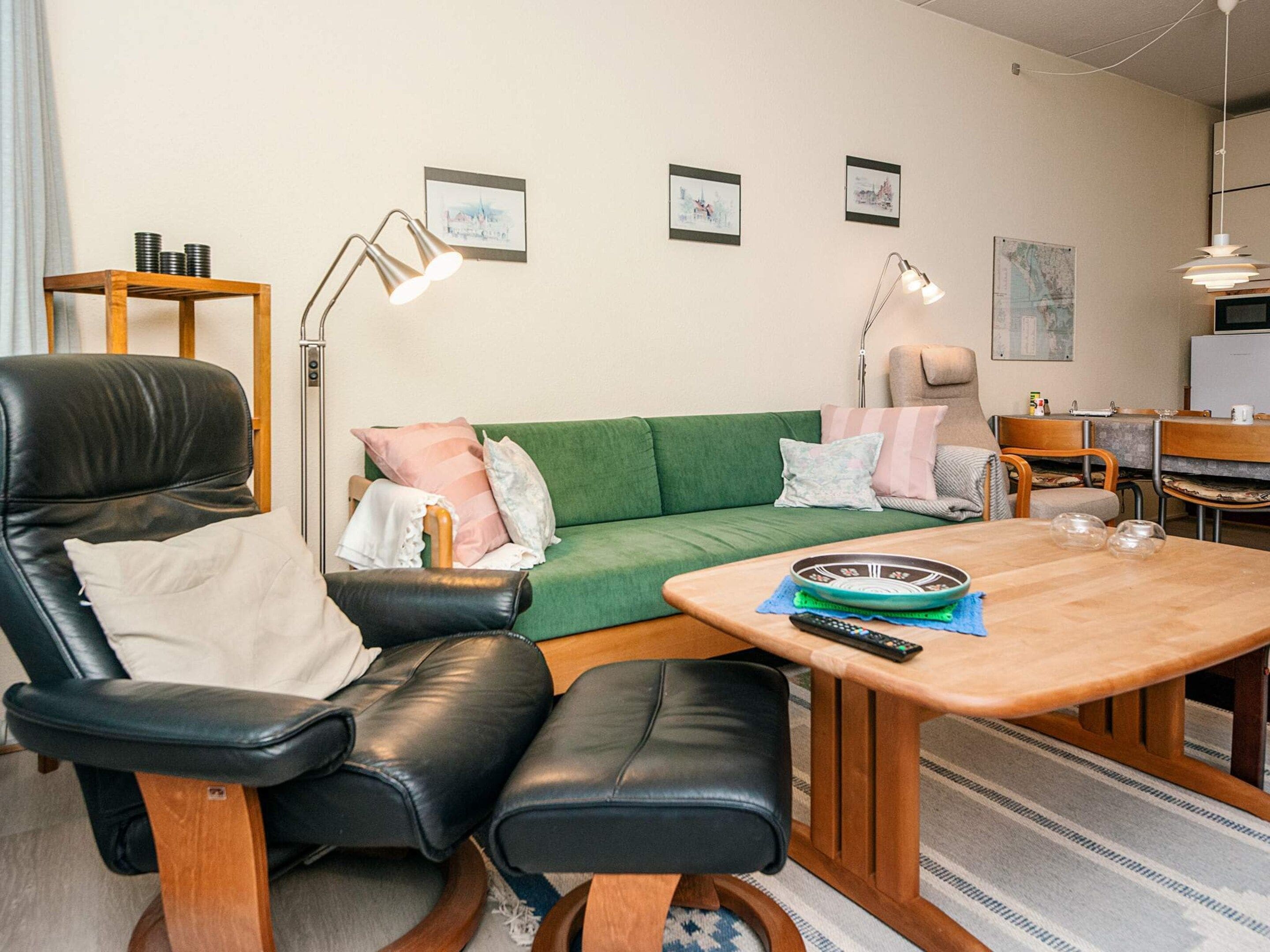 A modern living room with a green sofa, black leather chair, wooden coffee table, and a small side table with a lamp.