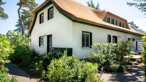 Ein zweistöckiges Haus mit einem Strohdach, umgeben von viel Grün.