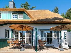 A building with a thatched roof, green trim, and large windows. There are outdoor tables and chairs, and umbrellas providing shade. - Beach House Dune 19 - Joy (Ostseebad Dierhagen)