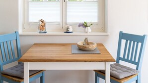 Ein Essbereich mit einem Holztisch und blauen Stühlen, einem Fenster mit weißen Jalousien und einer weißen Pendelleuchte.