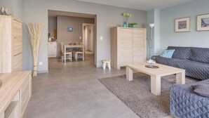 A modern living room with a sofa, a coffee table, and a dining area with chairs and a table. - Pleasant Apartment Near the Seafront (Blankenberge)