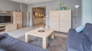 A modern living room with a TV, sofa, coffee table, and a kitchen in the background. - Pleasant Apartment Near the Seafront (Blankenberge)