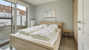 A bedroom with a bed, a small stool, a radiator, and a view of the outside. - Pleasant Apartment Near the Seafront (Blankenberge)